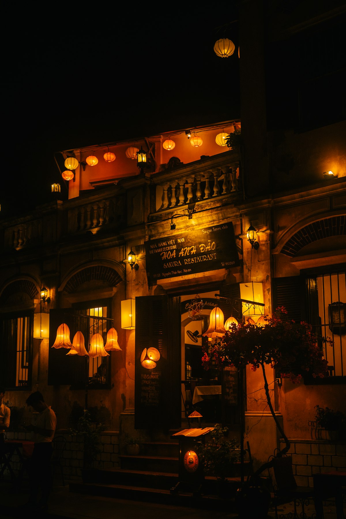 Hoi An December — lanterns illuminate an Ancient Town building at night, warm golden light glowing in the cool winter dark