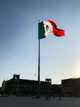 Mexican flag waving gently above a modern business district at sunset.