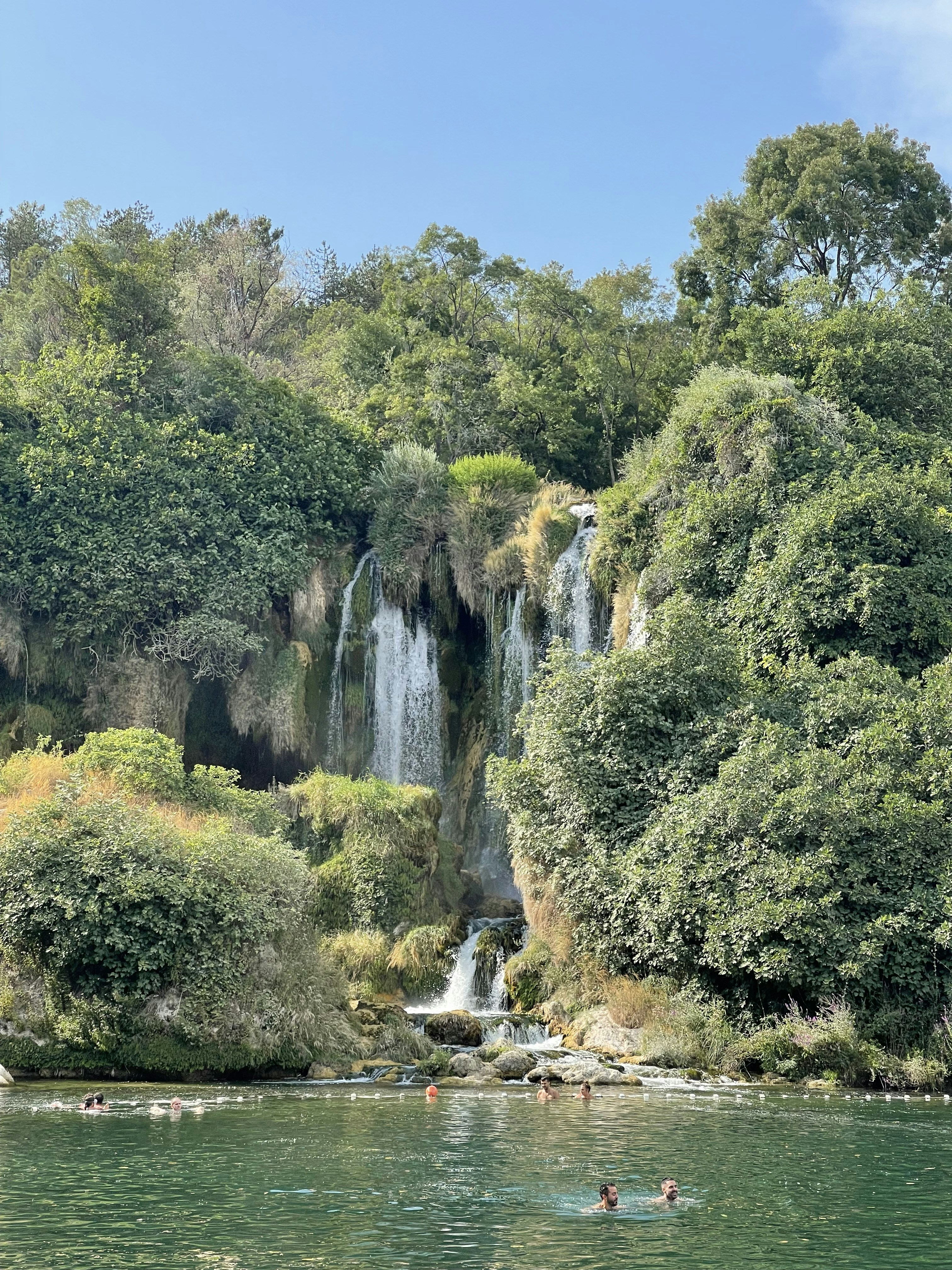 a group of people swimming in a river next to a waterfall