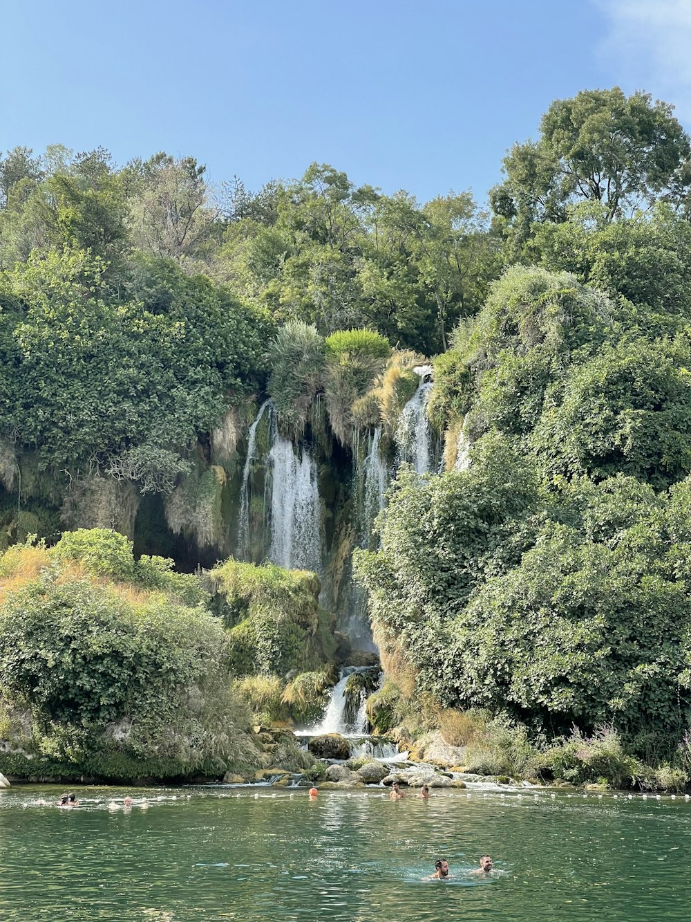 a group of people swimming in a river next to a waterfall