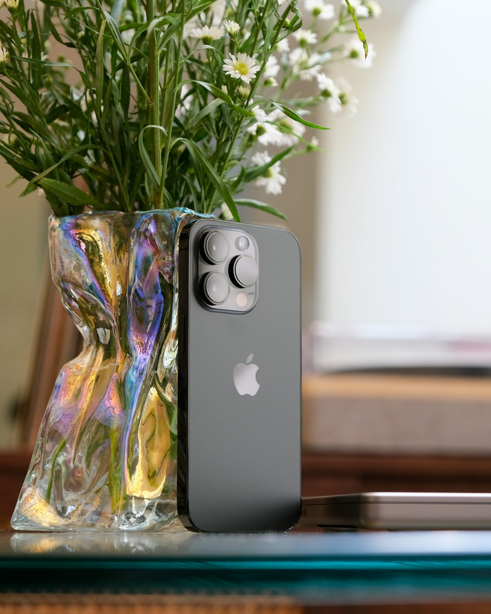 um estojo para iphone sentado em uma mesa ao lado de um vaso de flores