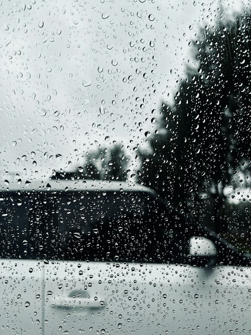 a rain covered window with a car in the background