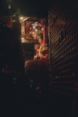 A serene statue of Buddha sits illuminated by warm, golden lights in a dimly lit, ornately decorated temple interior. Red lanterns hang from the intricately designed ceiling, casting a soft glow across the space.