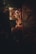 A serene statue of Buddha sits illuminated by warm, golden lights in a dimly lit, ornately decorated temple interior. Red lanterns hang from the intricately designed ceiling, casting a soft glow across the space.