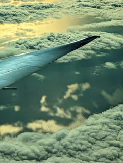 A scenic airplane wing view flying above fluffy white clouds at sunrise.