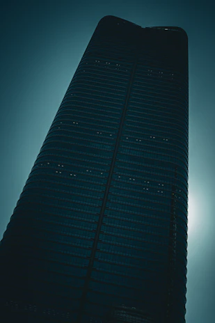 A sleek black architectural facade illuminated subtly by silver light, casting sharp, mysterious shadows.