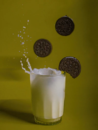Glass of creamy soy milk with a splash effect, set against a clean white background with green leaves.