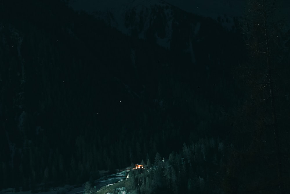 a night time view of a snowy mountain with a house in the distance