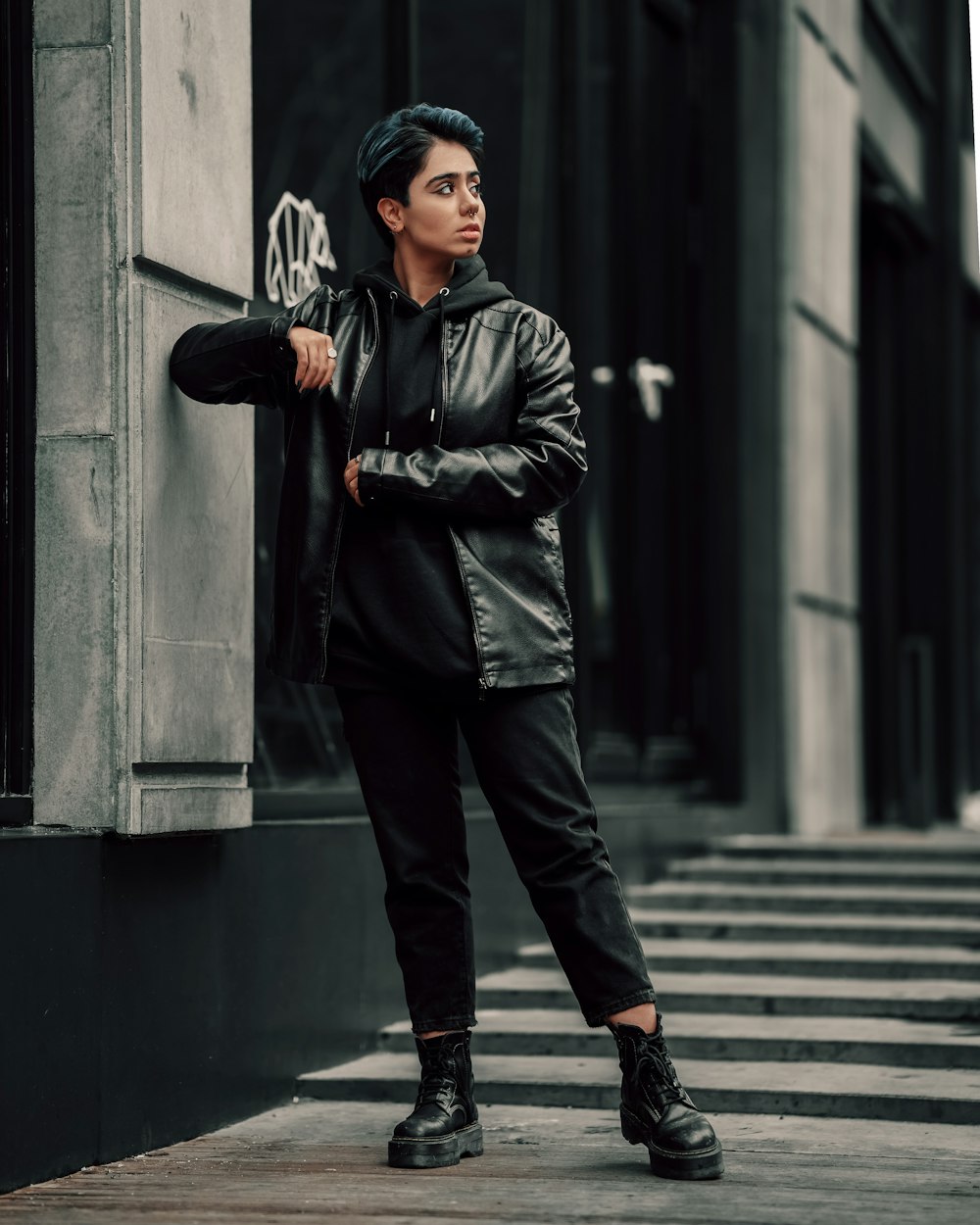 a young man leaning against a wall in a black leather jacket