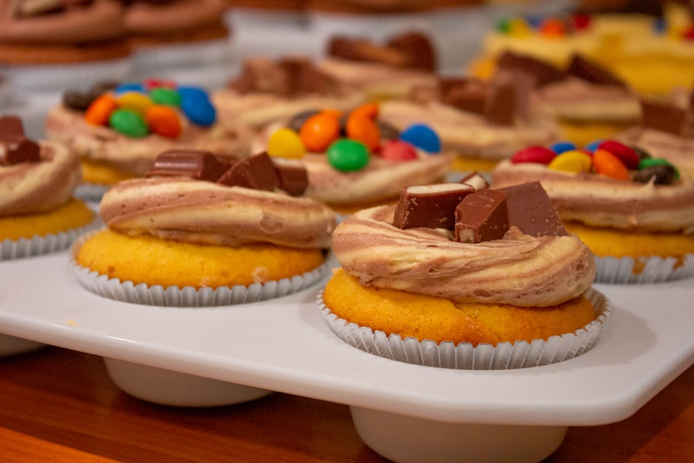 a tray of cupcakes with frosting and candy on top