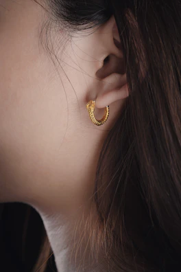 Elegant close-up of gold hoop earrings glinting near soft waves of chestnut hair.