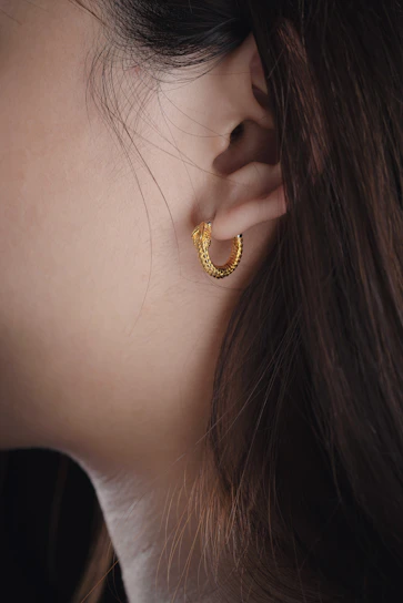 Minimalist shot of a woman’s ear adorned with sleek, modern gold hoop earrings