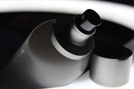 A close-up view of a spray bottle with its cap removed. The bottle has a sleek, matte black finish, and the nozzle is prominently displayed. The background contrasts with bright highlights, giving a modern and polished appearance.