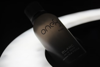 A silhouette of a perfume bottle with the brand name 'one' and the word 'BLANC' on it, set against a dark background with a soft, glowing light source beneath it, creating a moody and elegant atmosphere.