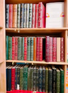 Stack of books with white, tan, and evergreen covers arranged on a wooden shelf