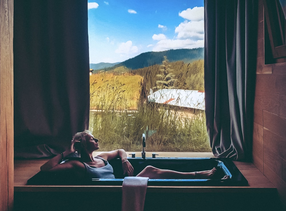 a woman sitting in a bathtub looking out a window