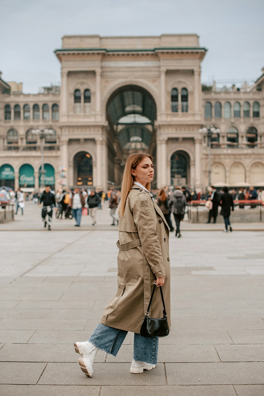 a woman in a trench coat is walking in front of a building