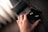 Hand holding a pair of compact wireless earbuds with a charging case on a wooden table.