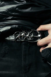 Close-up of a man’s hands adjusting a sleek leather belt over dark denim jeans.