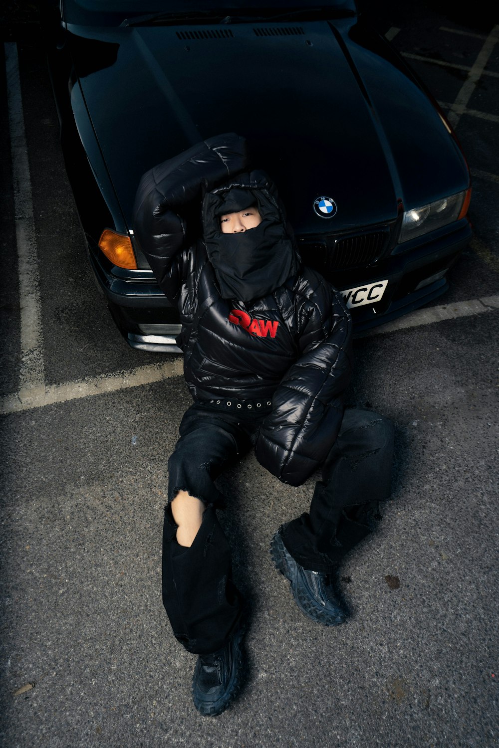 a person in a black jacket sitting in front of a black car