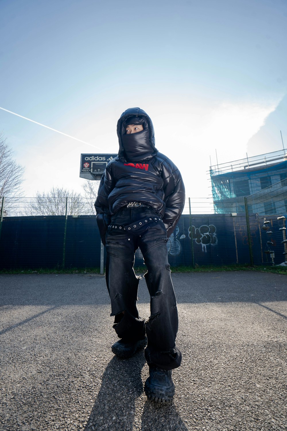 a person in a black jacket and black pants standing in a parking lot