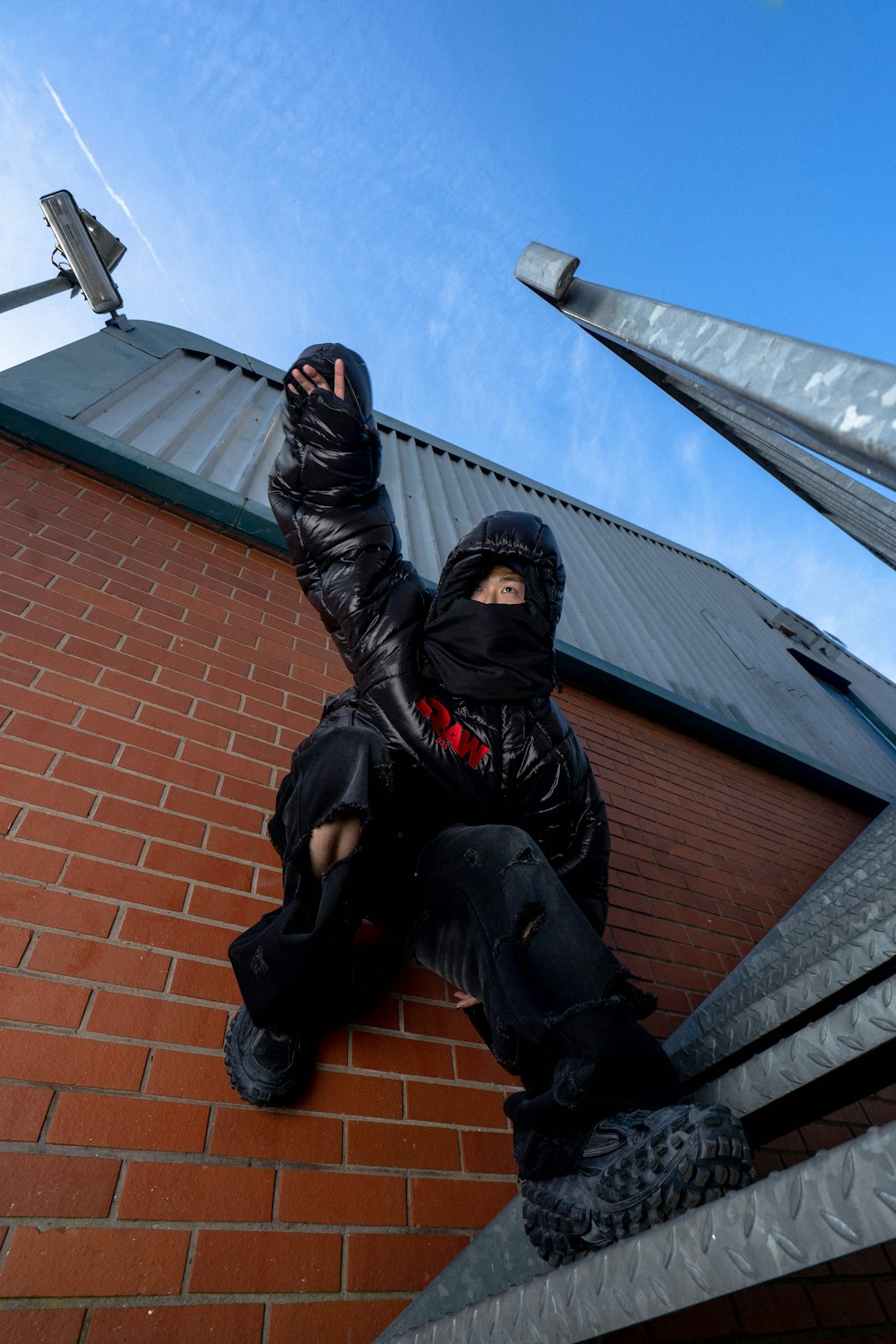 a man sitting on a brick wall with his hand up in the air