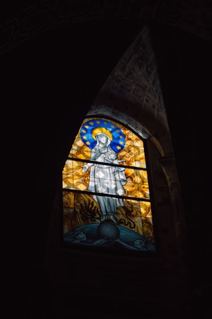 A serene image of a stained glass window featuring Saint Teresa of Calcutta with a glowing halo.