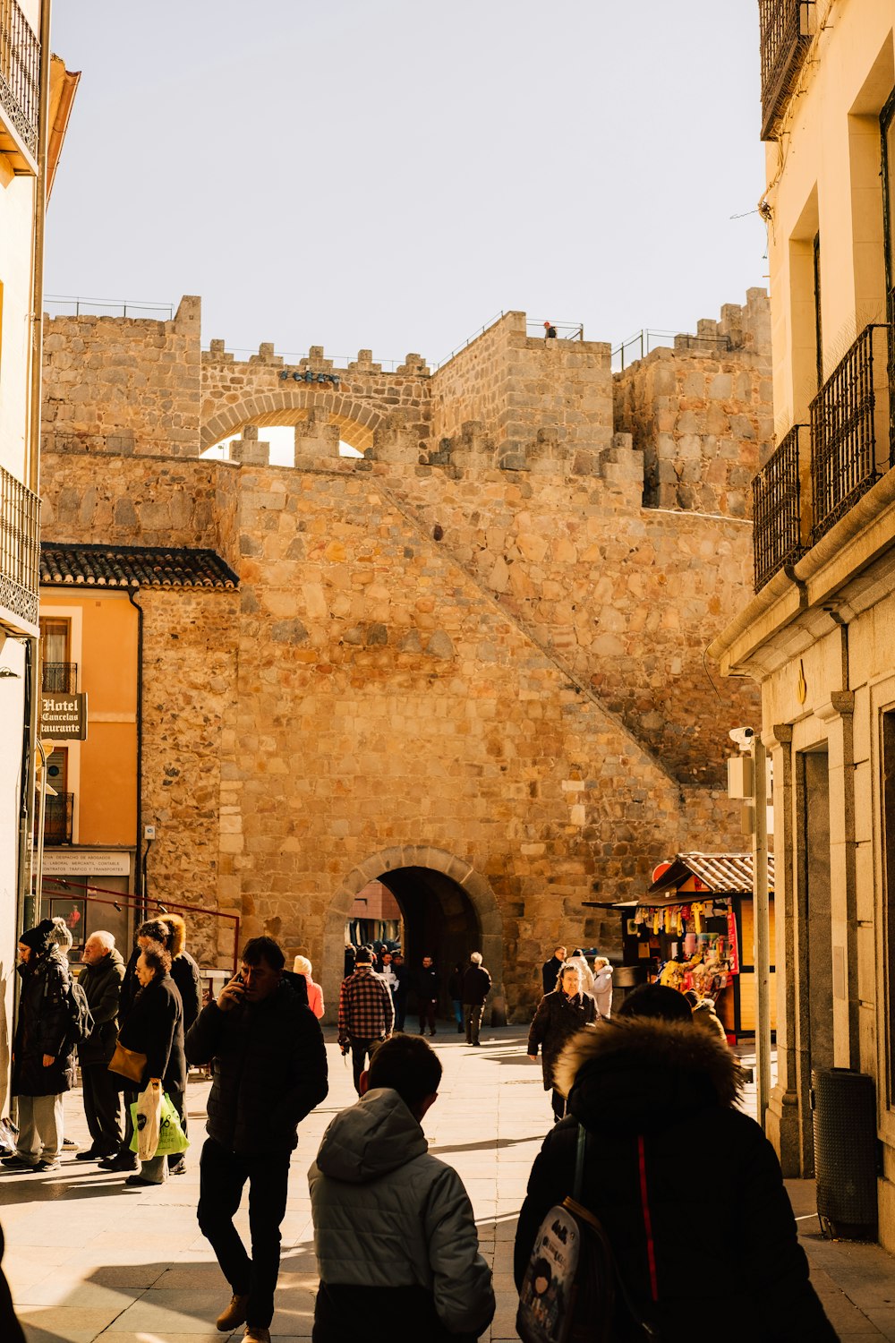 a group of people walking down a street next to a stone wall