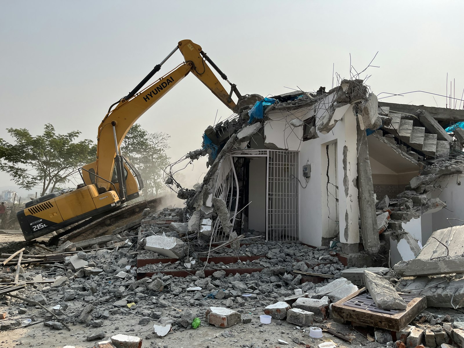 An excavator tearing through a partially demolished building, exposed structure and rubble in daylight