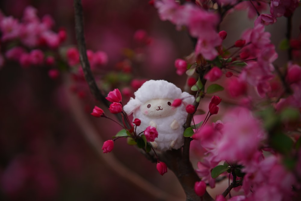 un animal en peluche est assis sur une branche d’un arbre en fleurs