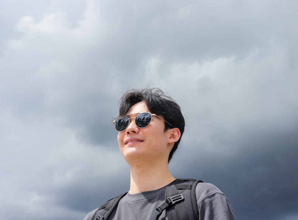 a man wearing sunglasses and a backpack looks up into the sky
