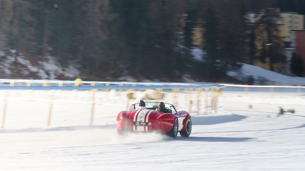a red car driving down a snow covered road