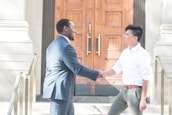A confident politician shaking hands with a compliance expert outside a government building.