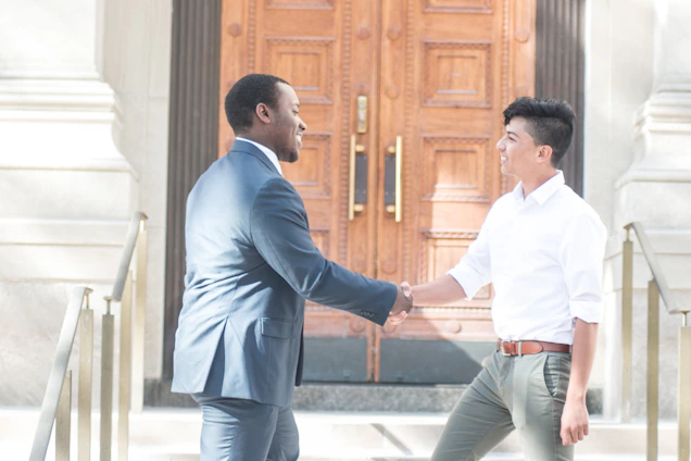 A warm handshake between a mortgage broker and a smiling couple in front of their new home under a clear blue sky.