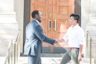A friendly agent shaking hands with a homeowner in front of a cozy house.