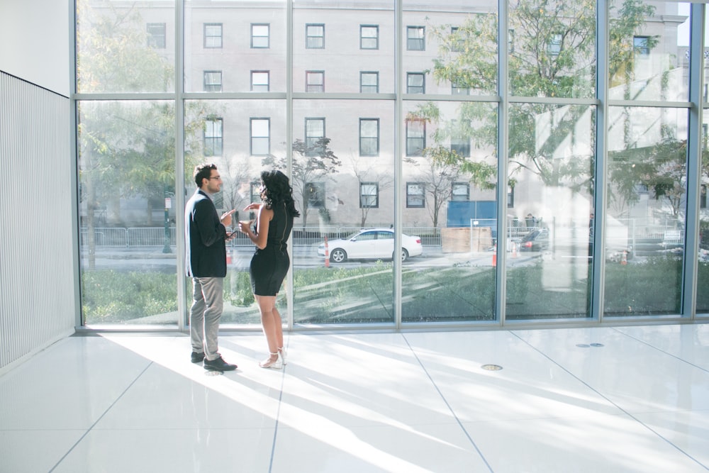 a man and woman standing in front of a large window