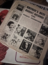 A vintage magazine page featuring an advertisement for budget records by Pickwick International. The page includes black and white images of various album covers, with titles such as 'HAIR', 'LOVE SONGS', and 'JOHNNY CASH'. Prominently displayed is the text 'BRITAIN'S BEST BUDGET RECORDS'. The page is placed on a surface that includes a partially visible red polka dot fabric.