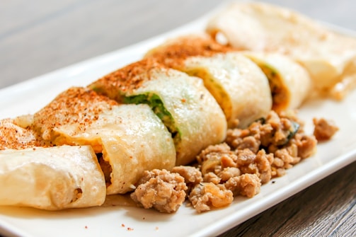 Chef's hands carefully rolling a kathi roll with a selection of spicy, marinated fillings.