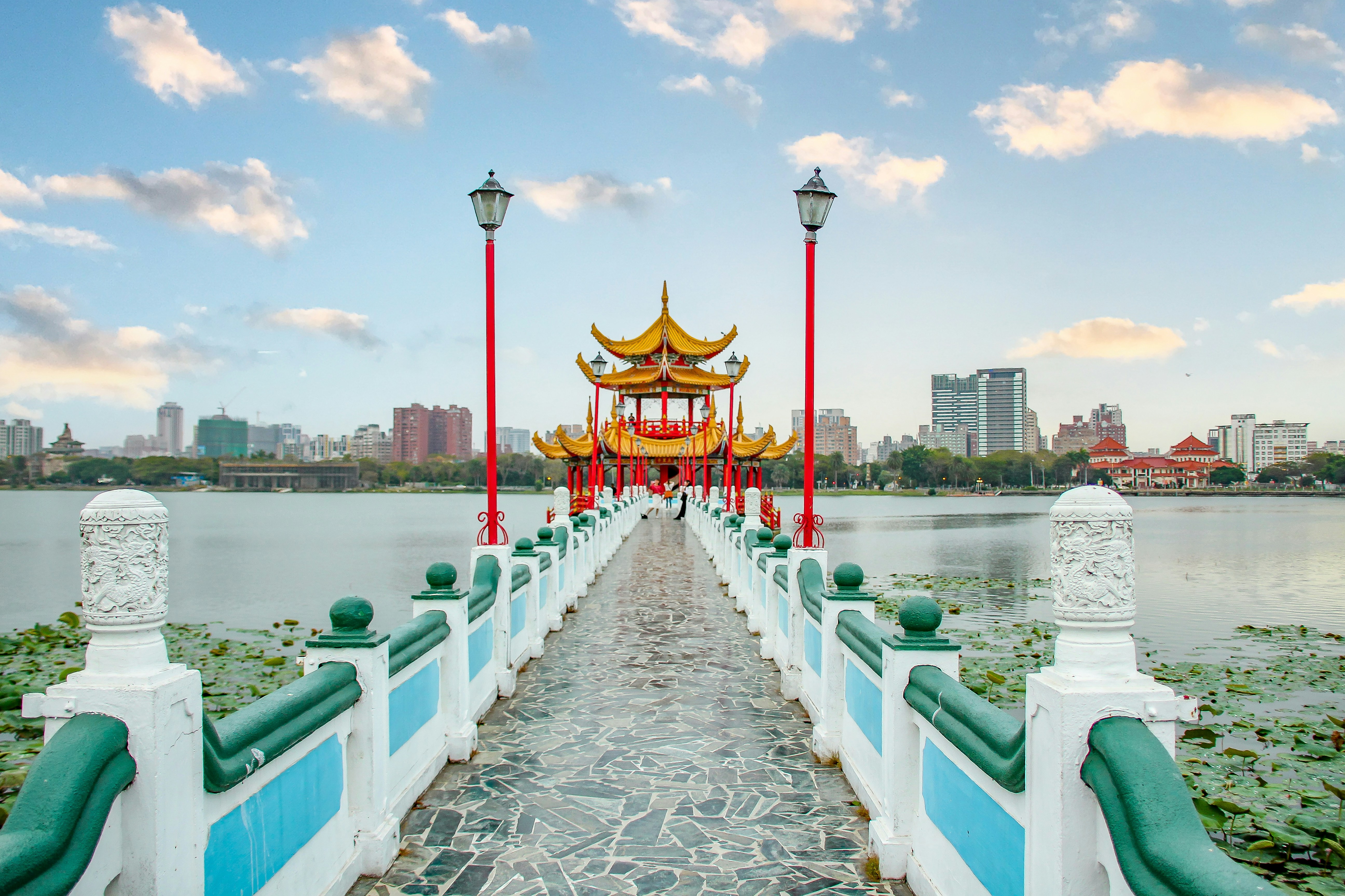 a bridge that is next to a body of water, Kaosiung dragon and tiger pagoda with the large dragon and pond and blue sky in the back