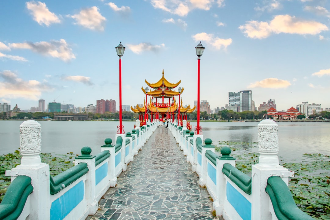 a bridge that is next to a body of water, Kaosiung dragon and tiger pagoda with the large dragon and pond and blue sky i