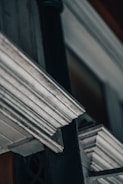 A close-up view of architectural details featuring ornamental cornices and moldings with a weathered, metallic appearance. The photo captures the intricate and linear design elements, creating a sense of depth and perspective.