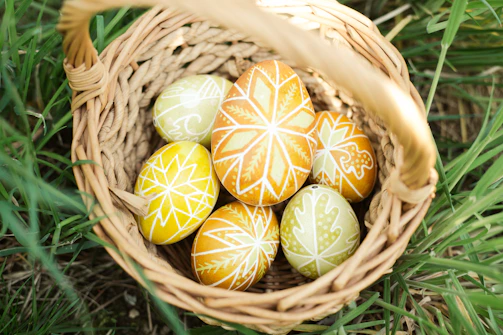 A basket overflowing with brightly painted Easter eggs resting on fresh, deep green grass.