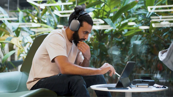 A person wearing headphones, working intently at a desk surrounded by plants and motivational quotes.