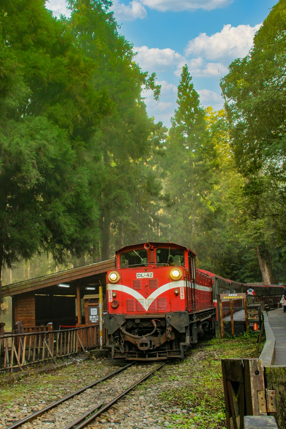 a red train traveling down train tracks next to a forest