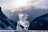 An intricately carved ice sculpture of an animal, possibly a reindeer, stands in the foreground against a backdrop of misty mountains and a cloudy sky. The ice is translucent and reflects the ambient light, adding a mystical quality.