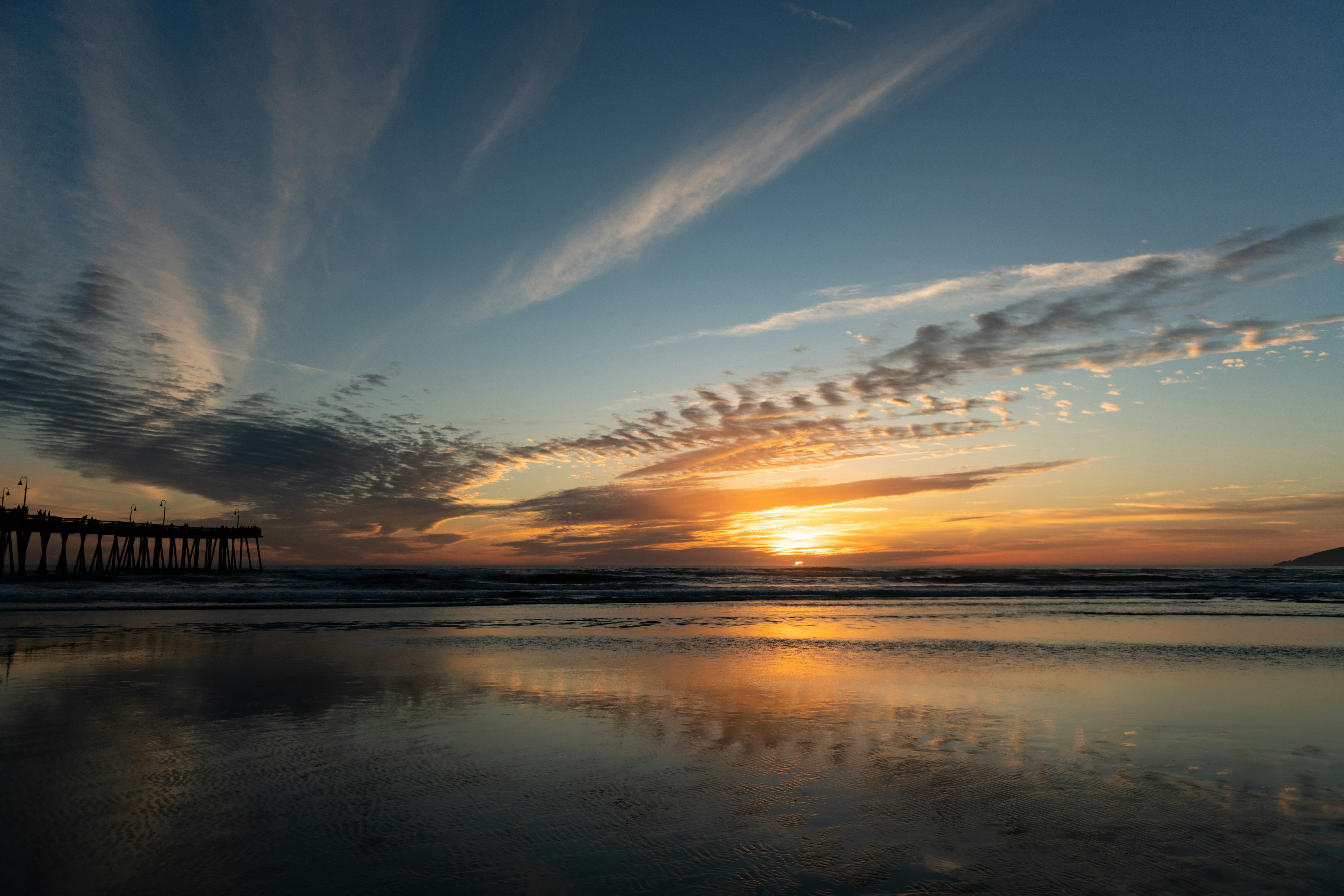 the sun is setting over a beach with a pier in the distance
