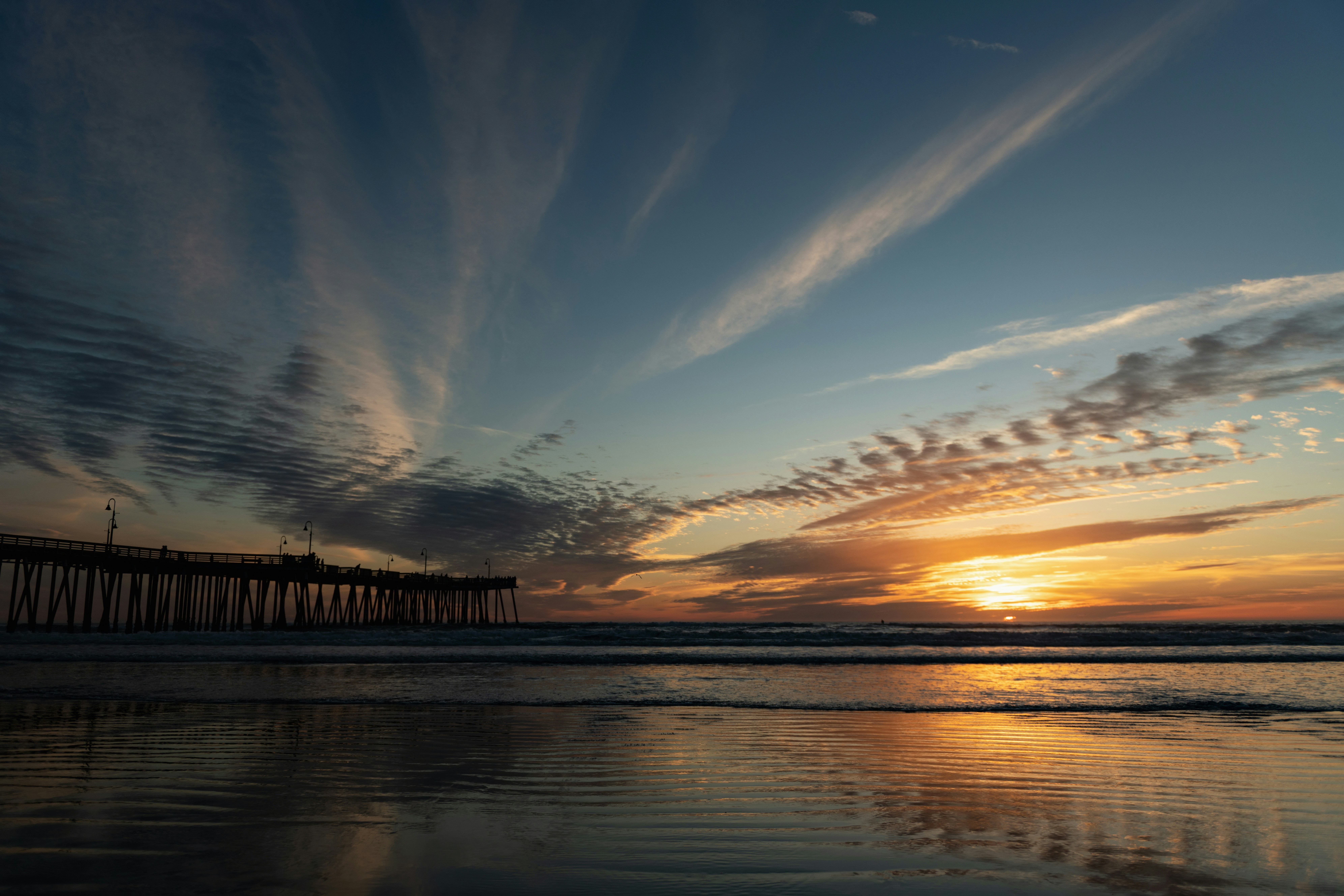 the sun is setting at the end of a pier