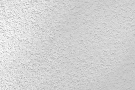 A close-up view of a textured white surface, possibly a plastered or stucco wall. The surface has a rough, uneven finish with small variations and grooves, creating a subtle pattern.