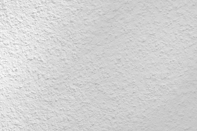 A close-up view of a textured white surface, possibly a plastered or stucco wall. The surface has a rough, uneven finish with small variations and grooves, creating a subtle pattern.