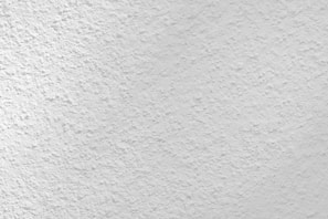 A close-up view of a textured white surface, possibly a plastered or stucco wall. The surface has a rough, uneven finish with small variations and grooves, creating a subtle pattern.